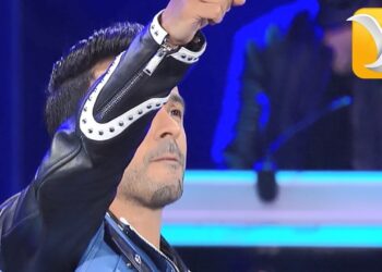 Cantante en escenario con chaqueta de cuero levantando el brazo bajo iluminación azul durante un concierto