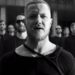 Vocalista en primer plano con varios músicos detrás en imagen en blanco y negro, ambiente dramático y estética de videoclip.