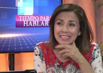 Retrato de una presentadora sonriente en un set de televisión con la pantalla del programa visible