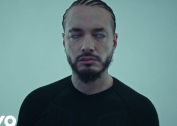 Retrato de un hombre con trenzas y barba sobre fondo neutro, mirada fija y estética minimalista