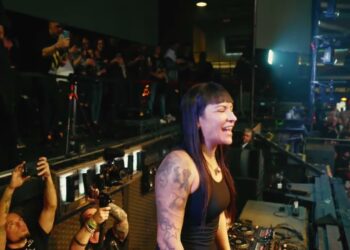 DJ femenina sonriente en cabina frente a una multitud y fotógrafos, ¿Cuánto cobra Fátima Hajji? Descubre su tarifa y más detalles