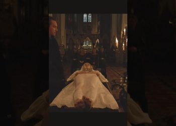 Descubre el secreto de Jane Seymour para lucir joven a los 70 años, ¡no te lo querrás perder! escena de una figura femenina acostada en túnica blanca sobre una mesa o ataúd en el interior de una iglesia gótica con velas encendidas y asistentes al fondo
