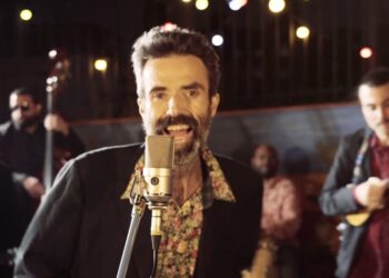 Cantante principal frente a un micrófono rodeado de músicos en un ambiente de estudio íntimo, Jarabe de Palo: descubre sus raíces y legado musical en España.