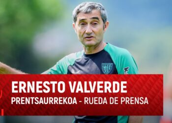 Entrenador señalando durante un entrenamiento con rótulo de rueda de prensa, sugiriendo un vistazo a su hogar y estilo de vida.