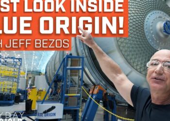 Hombre calvo con gafas de seguridad señalando un gran módulo esférico en el interior de una nave industrial dedicada a la fabricación de cohetes