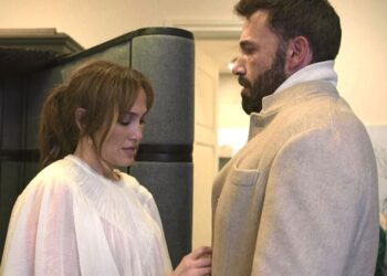 Mujer con blusa blanca y hombre con abrigo beige frente a frente en un pasillo interior; Cuántos hijos tiene Jennifer Lopez: descubre su familia y más