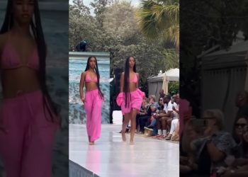 Dos modelos gemelas desfilan con conjuntos rosas en una pasarela al aire libre frente a un público