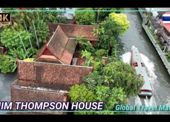 Descubre la fascinante historia de la casa de Jim Thompson en Bangkok en una vista aérea de su casa-museo tradicional junto a un canal rodeada de vegetación y embarcaciones.