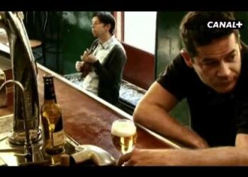 Hombre apoyado en la barra con una cerveza y un músico tocando al fondo; ¿Qué fue de Jorge Sanz? Su vida, retos y secretos revelados.