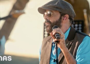 Descubre de dónde es Juan Luis Guerra y su legado musical: cantante con gorra plana, gafas de sol y micrófono en escenario al aire libre.