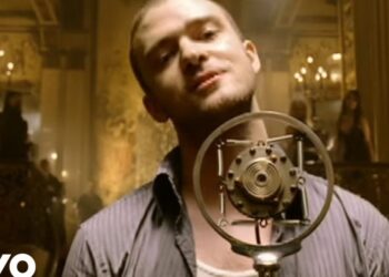 Hombre cantando frente a un micrófono antiguo en un salón dorado y elegante, Las parejas más icónicas de Justin Timberlake y sus historias ocultas