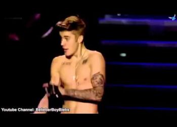 Cantante masculino en concierto con torso descubierto, tatuajes visibles y guantes