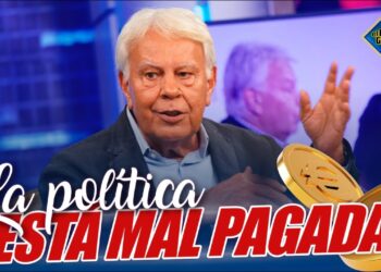 Hombre mayor en plató televisivo con el texto 'La política está mal pagada' y monedas de euro que ilustran un debate sobre salarios y remuneraciones.