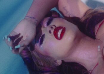 Retrato cinematográfico de una artista recostada con maquillaje glamuroso, labios rojos con purpurina y pestañas dramáticas