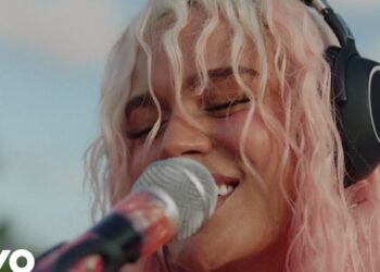 Cantante con cabello rosado y auriculares cantando frente a un micrófono