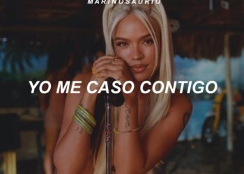Mujer rubia con micrófono en un escenario tropical, mirada directa y el texto YO ME CASO CONTIGO superpuesto.