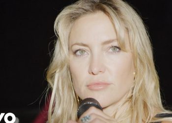 Primer plano de mujer rubia sosteniendo un micrófono con mirada serena sobre fondo negro