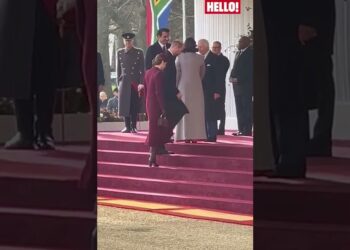Mujer con abrigo claro y otra con abrigo burdeos subiendo una escalinata ceremonial frente a guardias y asistentes