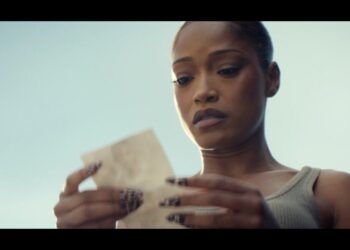 Mujer mirando detenidamente un papel con expresión concentrada, uñas decoradas y peinado recogido en un primer plano