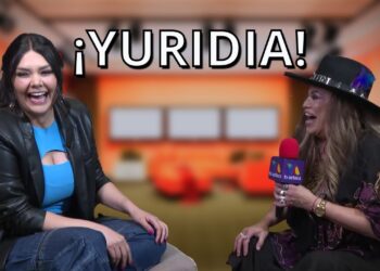 Dos mujeres riendo en una entrevista televisiva con micrófono y fondo de estudio, texto promocional: ¿Qué fue de Yuridia? Descubre su vida y secretos actuales