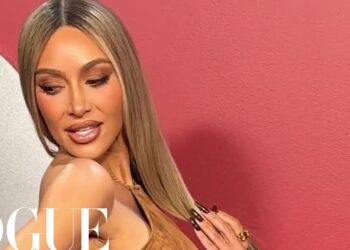 Retrato glamuroso de una persona no identificada con cabello largo y maquillaje impecable frente a un fondo rosa