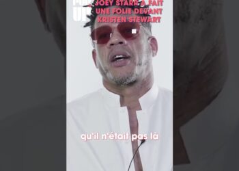 Retrato en vertical de un hombre con gafas de sol rosadas y camisa blanca hablando frente a cámara en estilo editorial