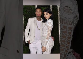 Pareja posando en un evento nocturno, mujer con vestido blanco de crochet y hombre con traje claro.