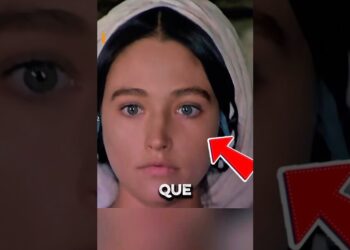 Rostro frontal de una mujer joven con pañuelo blanco en la cabeza y una flecha roja señalando su mejilla, con el texto sobreimpreso 'QUE'.