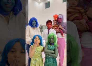 Familia en interior con caras pintadas y pelucas de colores posando junto a niños pequeños en un ambiente hogareño