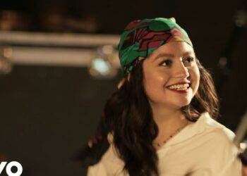 Mujer sonriente con pañuelo colorido en un pequeño escenario, ¿Qué fue de Mocedades? La historia y legado del icónico grupo español