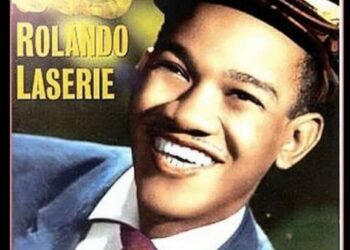 Retrato retro de un hombre sonriente con traje y gorra en un póster musical vintage; Descubre el impactante nuevo drama de 8 episodios que todos están viendo en Netflix de un solo tirón