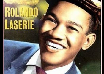 Retrato retro de un hombre sonriente con traje y gorra en un póster vintage; Descubre la nueva serie de thriller llena de escándalos con tus estrellas favoritas de The Diplomat y Slow Horses