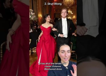 Mujer con vestido rojo de gala y acompañante de etiqueta en un elegante salón con candelabros