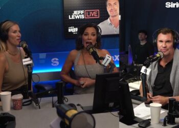 Mujer con expresión sorprendida y divertida en un estudio de radio junto a dos presentadores, reaccionando tras la inesperada cancelación de 'RHONY'.