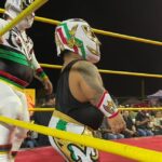 Luchadores enmascarados en un ring nocturno con cuerdas amarillas y público alrededor; ¿De dónde es Kane de WWE? Descubre su origen y trayectoria