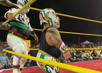 Luchadores enmascarados en un ring nocturno con cuerdas amarillas y público alrededor; ¿De dónde es Kane de WWE? Descubre su origen y trayectoria