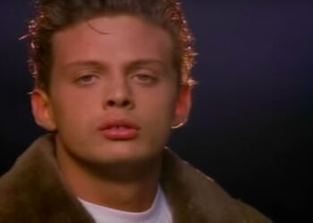 Retrato en primer plano de un cantante joven con chaqueta de cuello de piel sobre fondo oscuro