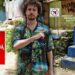 Hombre con camisa tropical señalando junto a carteles urbanos: creador de contenido popular descubre su sorprendente fortuna y ganancias