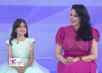 Mujer adulta y niña sonriendo sentadas en un set de televisión con vestidos elegantes y fondo violeta
