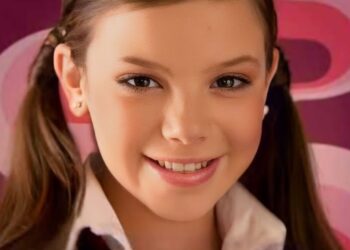 Niña sonriente con coletas en primer plano sobre fondo rosa.