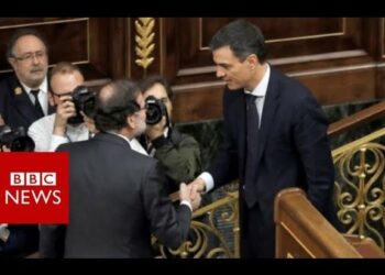 Dos políticos en traje dándose la mano en un hemiciclo con fotógrafos de fondo; ¿Cuánto cobra Mariano Rajoy? Descubre su sueldo actual y más