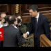 Dos políticos en traje dándose la mano en un hemiciclo con fotógrafos de fondo; ¿Cuánto cobra Mariano Rajoy? Descubre su sueldo actual y más