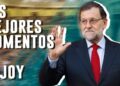 Hombre mayor con traje oscuro y corbata roja saludando con la mano alzada junto a un fondo borroso y texto grande en mayúsculas