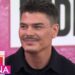 Hombre sonriente en un plató televisivo con fondo rosa y logo de programa, ¿De dónde es Sephora? Descubre la historia detrás de la marca