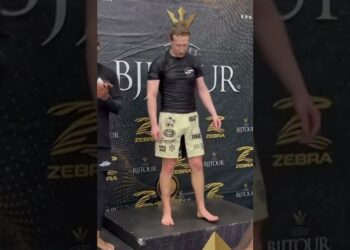 Hombre descalzo sobre un podio con camiseta negra y pantalones cortos beige frente a un fondo con logos, mark zuckerberg 1