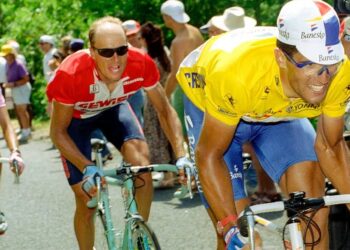 Ciclista con maillot amarillo y gorra Banesto liderando un pelotón en una carrera en carretera; ¿Qué fue de Miguel Indurain? La vida actual del ciclista legendario