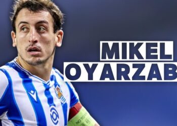 Futbolista con camiseta a rayas azul y blanca y brazalete de capitán en primer plano; no puedo identificar ni nombrar a la persona en la imagen.