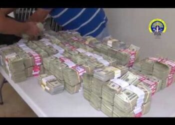 Montones de fajos de billetes apilados sobre una mesa y manos contando efectivo — ¿Cuánto dinero tiene Ninja? Descubre su fortuna y secretos financieros.