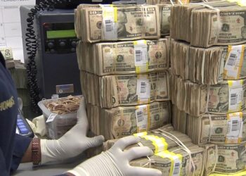 Montones de fajos de dólares apilados y etiquetados sobre un escritorio mientras unas manos enguantadas los manipulan, Patrimonio de Piqué: ¿Cuánto realmente tiene el exfutbolista?