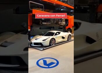 Ferrari blanco posado en una plataforma metálica dentro de un taller junto a un camión naranja; Fortuna del PSG: descubre su dinero y secretos financieros.